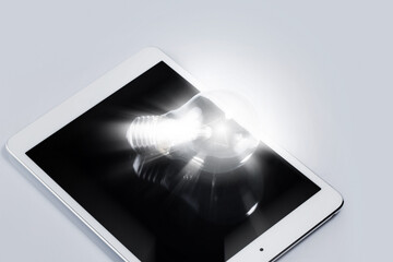 Closeup of light bulb lying on white tablet computer