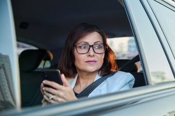 Portrait of middle-aged business woman in car in back passenger seat.