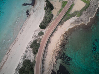 Bird's eye view of the road passing along the shore surrounded by turquoise water.