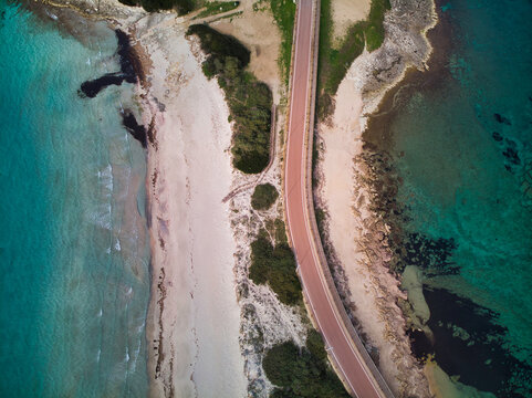 Aerial drone view of road passing trough a idyllic isthmus neck with sandy beach and vibrant blue sea, (Rena di ponente e levante) Sardinia.