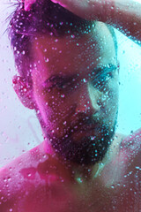 Fototapeta premium Portrait of handsome young man captured through wet glass in colorful light