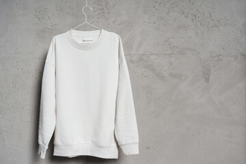 White sweatshirt hanging on the thin metallic hanger against a concrete wall