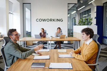 Side view portrait of HR manager talking to young man at job interview in office, copy space