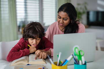 Fototapeta premium Indian mother with little son using laptop and having online school lesson at home.