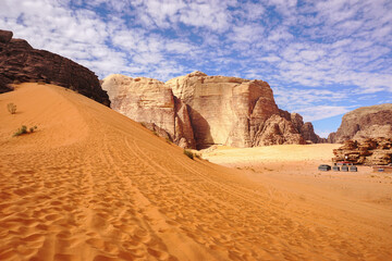 Fototapeta na wymiar red sand dune surrounded by wind-beaten mountains, beautiful cloudy sky, Wadi Rum desert, Jordan 