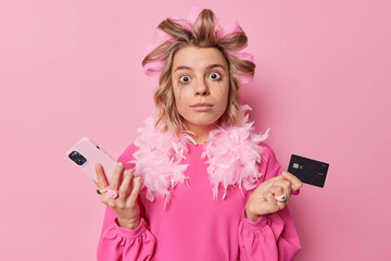 Photo of puzzled woman holds smartphone and credit card doesnt know how to install new application...