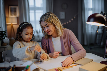 Mother helping her daughter with homework, drawing a circle with comasses in evening at home.