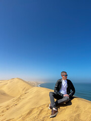 A young man sitting at sandy dunes on the seashore. Sandwich Harbour in Namibia