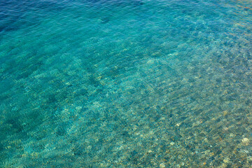 Fototapeta na wymiar Texture of transparent turquoise blue rippling water of the sea with small stones under the surface