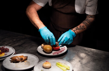 Chef's hands in gloves serving and decorating meal in restaurant kitchen
