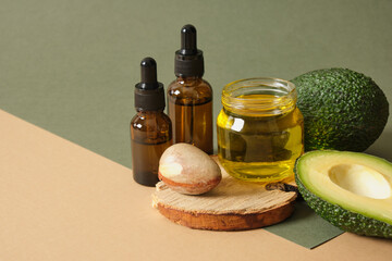 a jar of oil, a sliced avocado, an avocado seed and two amber glass dropper bottles on a wooden...