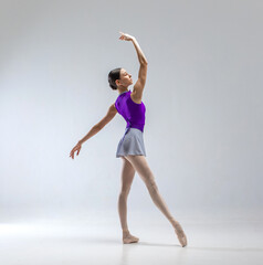 Young and beautiful ballerina in purple ballet leotard and grey skirt. She wears ballet pointe...