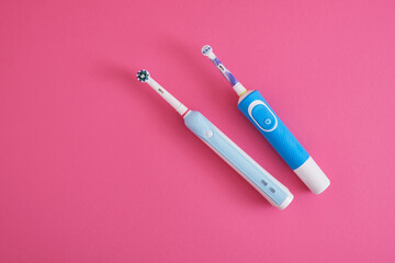 Fototapeta premium two electric blue toothbrushes on bright pink background oral hygiene concept