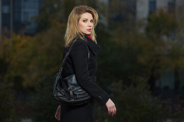 Young woman in black coat with leather handbag