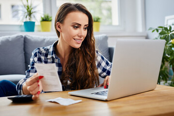 Smiling young woman calculating home finance on laptop