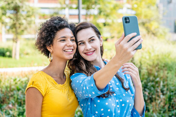 Happy diverse ladies taking selfie on smartphone during weekend in park