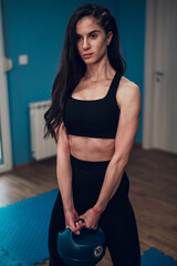 Fototapeta na wymiar Portrait of a young woman holding a kettlebell while training in the gym