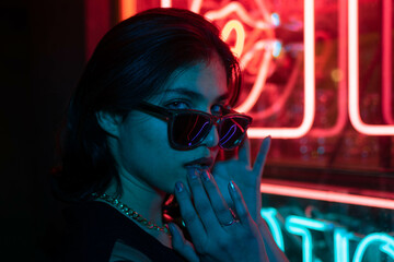 Street fashion young girl with sunglasses, neon light red blue, nightlife and trendy lifestyle