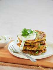 Close-up of a stack of roasted vegetable fritters served on a plate with Greek yogurt cream and cucumber, tzatziki and parsley on top