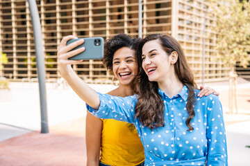 Cheerful diverse girlfriends taking selfie on street on sunny day