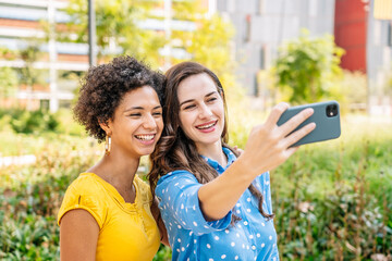 Delighted young multiracial women taking selfie on smartphone in city park