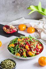 Fruit vitamin salad of pomegranate, tangerine, arugula and pumpkin seeds in a plate on the table. Organic vegetarian food.  Vertical view