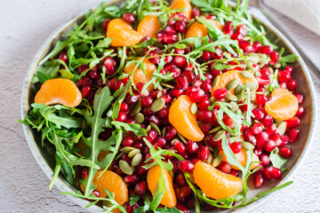 Fruit vitamin salad of pomegranate, tangerine, arugula and pumpkin seeds in a plate on the table....