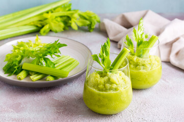 Two glasses with fresh celery smoothie and cooking ingredients on the table. Vegetarian detox diet...