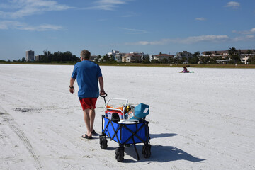 A rear view of Caucasian man pulling a wagon on the beach. Siesta Key Beach, Sarasota, Florida, USA. © Supinda Duke-Aiton