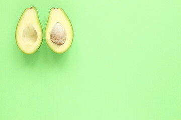 Two halfs of avocado with and without seed on green background. Top view.