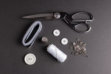 Sewing kit showing scissors, white buttons, tape measure, white thread, needle and thimble on black background.