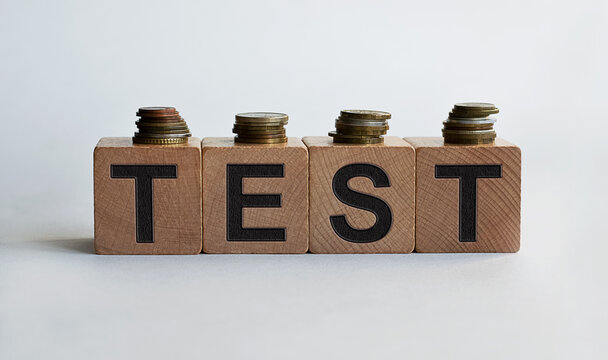 TEST inscription on wooden cubes, together with coins, isolated on white background, business and finance concept.