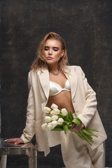 Young blonde woman with perfect makeup and wet hair effect in white formal pantsuit with unbuttoned...
