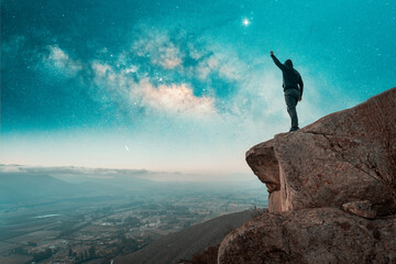 person silhouette on the top of the mountain with hand up with Milky Way background