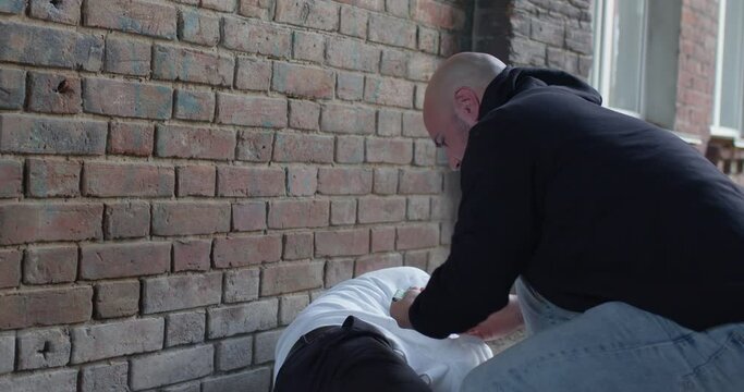 Aggressive robber beats frightened male and steal the money at daytime at street. Stranger threatening young black man. Male bandit wear black hoodie. Concept of robbery. City daytime