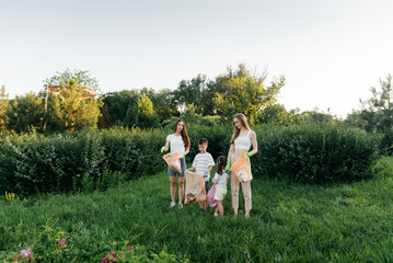 Obraz premium A group of adults and children together at sunset is engaged in garbage collection in the park. Environmental care, waste recycling. Sorting garbage.