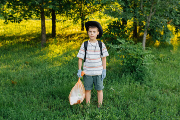 A seven-year-old boy at sunset is engaged in garbage collection in the park. Environmental care,...