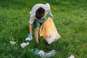A seven-year-old boy at sunset is engaged in garbage collection in the park. Environmental care, recycling.
