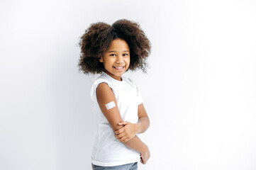 African American cute little girl, preschooler, with a band-aid on her shoulder, received a...
