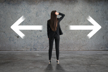 Back view of businesswoman with two arrows in concrete interior. Different direction and choice concept.