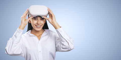 Virtual reality concept: smiled young woman in light shirt with VR headset on her head on light blue background with copyspace, mockup