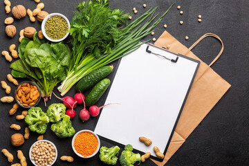 Concept: Purchase healthy clean food. Protein source for vegetarians: vegetables, nuts and legumes top view on a black background with a paper bag and a white notebook for a list of products.
