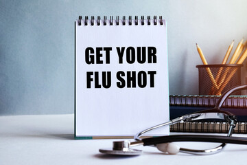 GET YOUR FLU SHOT - written on a notepad. Doctor's workplace. Work table with medical equipment and office supplies. Medical concept.