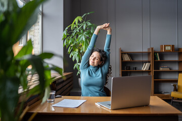 Happy businesswoman warming up body and muscles at workplace, feeling satisfied with work done, smiling female employee resting from computer screen. Well-being, productivity and happiness at work