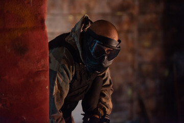 Paintball player in mask who is aiming in opponents at paintball arena. Selective focus