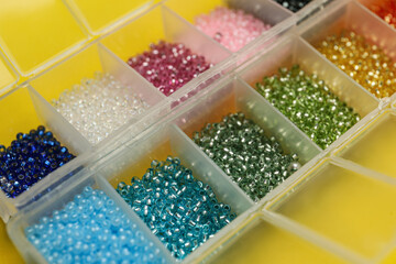 Organizers with variety of colorful beads on yellow background, closeup