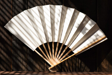 Old japanese folding fan on old wood background and hard shadows.