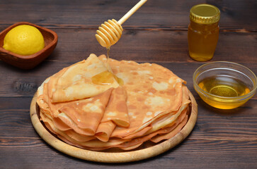 honey pours from a dipper onto a stack of thin pancakes for the Maslenitsa holiday