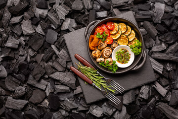 Frying pan with barbecue vegetables on a stone cutting board on coals. Top view.