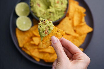 Closeup of woman hand with tortilla chips or nachos with fresh tasty guacamole dip